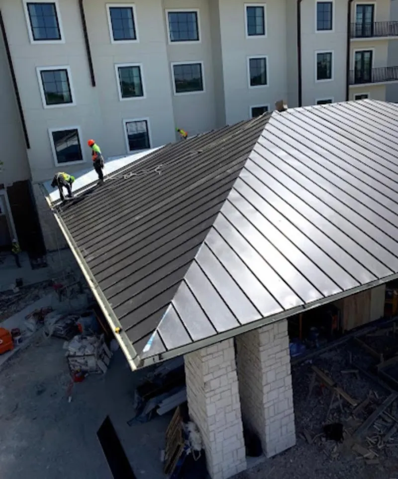 Crew installing standing seam metal roof panels on a commercial project in Oneida